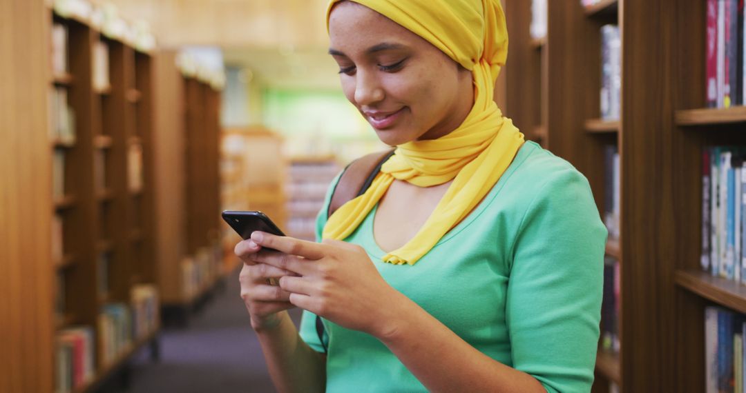 Young Woman Using Smartphone in Library, Wearing Yellow Headscarf - Free Images, Stock Photos and Pictures on Pikwizard.com