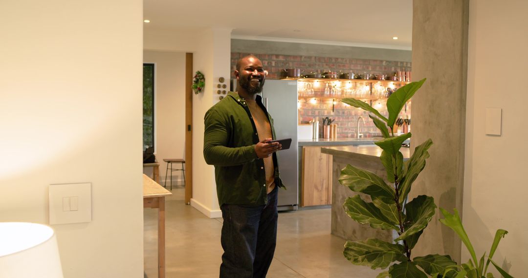African American man smiling while holding smartphone in modern open-plan kitchen