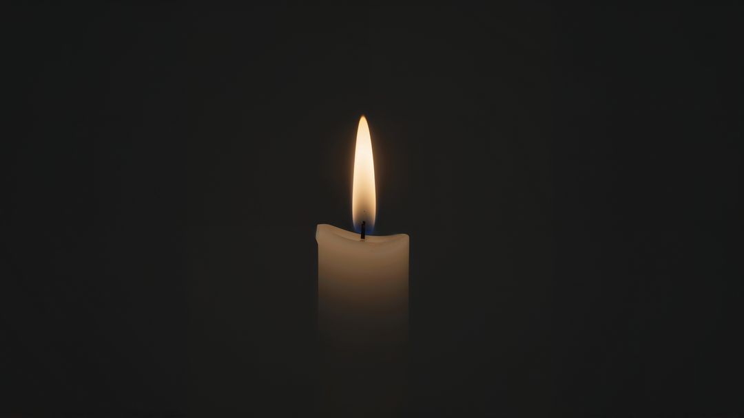 Glowing candle flame against black background for contemplative ambience and condolences