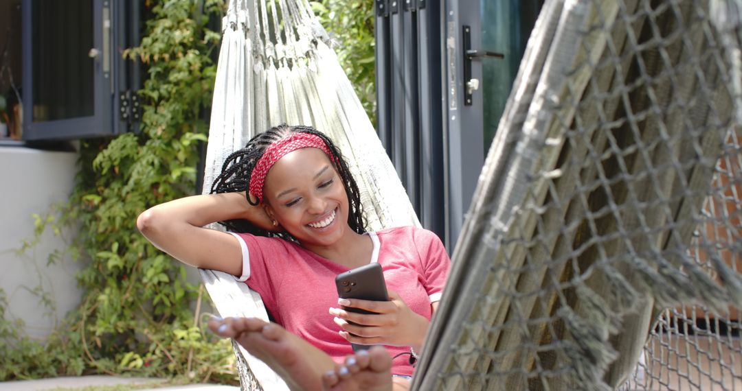 Young Woman Relaxing in Hammock with Smartphone in Sunny Garden