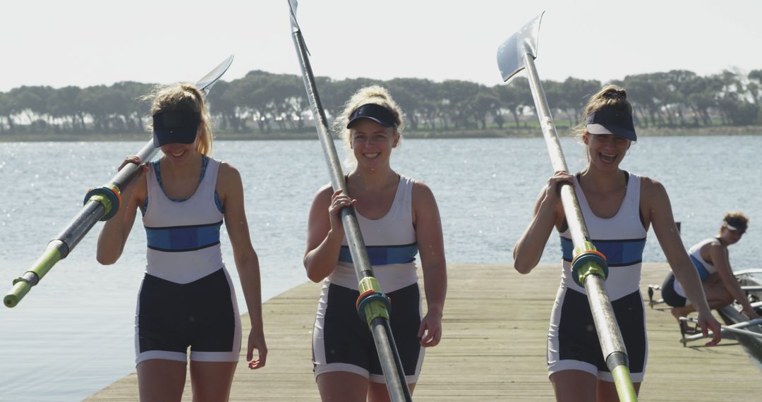 Female Rowers Carrying Oars on Sunny Lakeside Dock - Free Images, Stock Photos and Pictures on Pikwizard.com