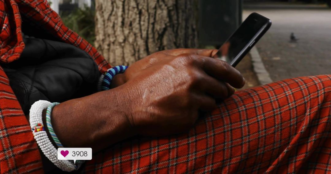 Man scrolling smartphone wearing red plaid pants and beaded bracelets on park bench