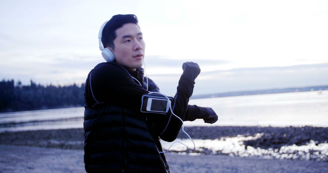 Man stretching with headphones on beach at sunrise - Free Images, Stock Photos and Pictures on Pikwizard.com