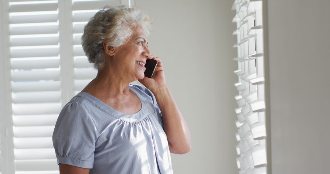 Senior Woman Talking on Mobile Phone by Window - Free Images, Stock Photos and Pictures on Pikwizard.com