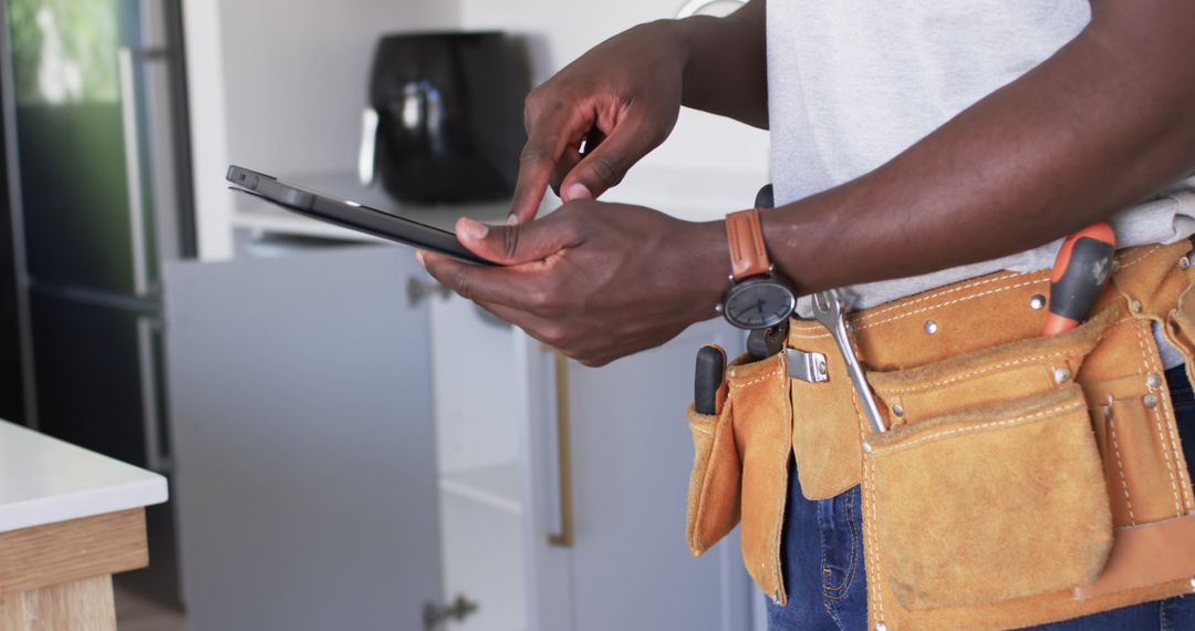 Handyman Checking Tablet with Tool Belt in Modern Kitchen