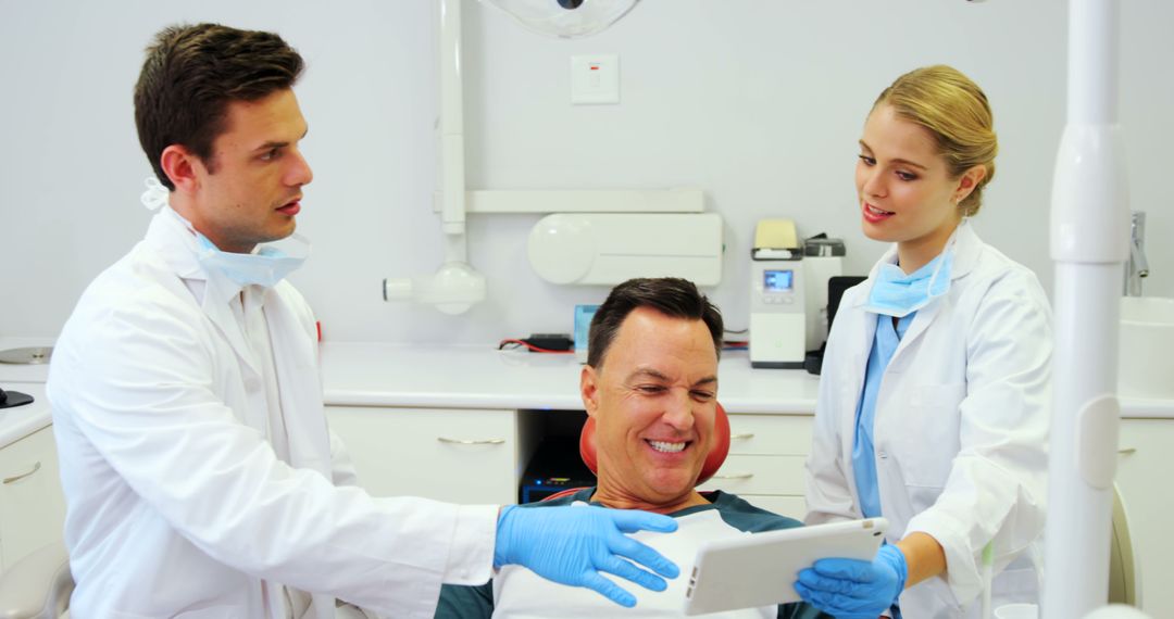 Dentist and Assistant Showing Tablet to Smiling Patient in Dentist Office - Free Images, Stock Photos and Pictures on Pikwizard.com