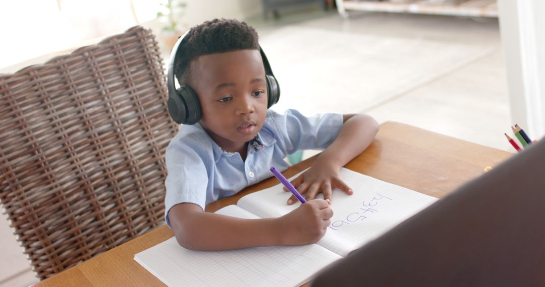 Focused Young Boy Wearing Headphones Writing in Notebook at Table - Free Images, Stock Photos and Pictures on Pikwizard.com