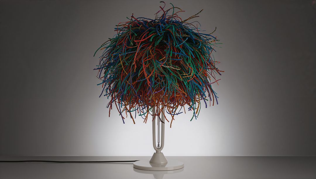 Multicolor Pom-Pom Table Lamp Casting Soft Halo on Gray Wall, Glossy White Base, Tangled Shade