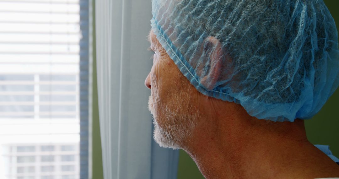 Elderly Patient Wearing Surgical Cap Looking Out Hospital Window - Free Images, Stock Photos and Pictures on Pikwizard.com