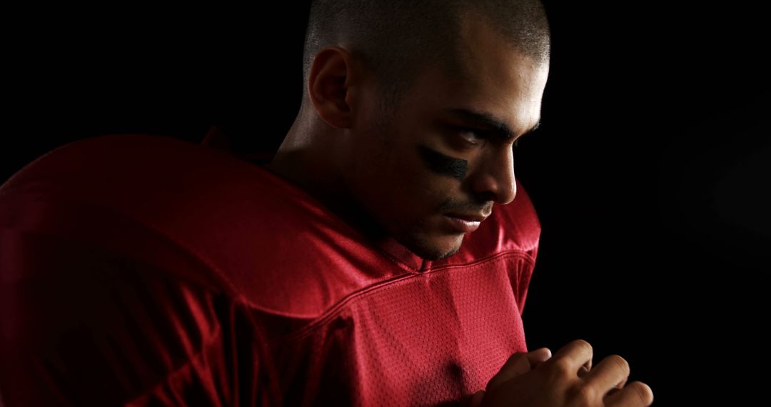 Focused Football Player in Red Jersey Preparing for Game on Black Background - Free Images, Stock Photos and Pictures on Pikwizard.com