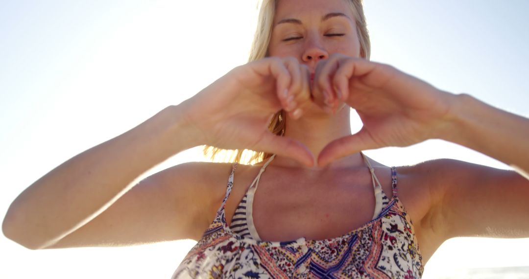 Blonde Woman Forming Heart Shape with Hands Against Sunlight - Free Images, Stock Photos and Pictures on Pikwizard.com