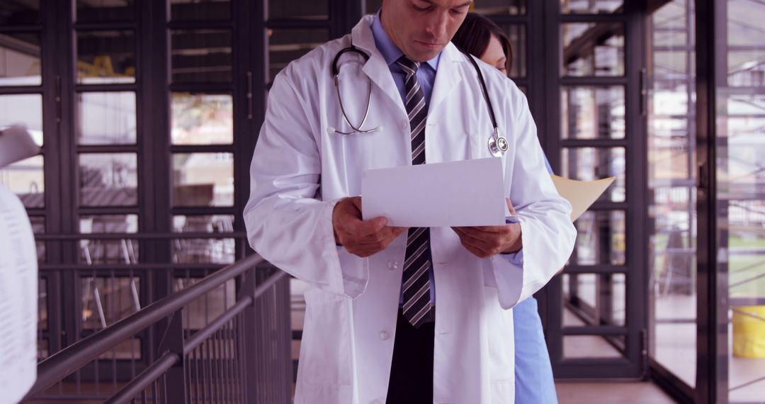 Focused Doctor Reviewing Medical Reports in Hospital Corridor - Free Images, Stock Photos and Pictures on Pikwizard.com