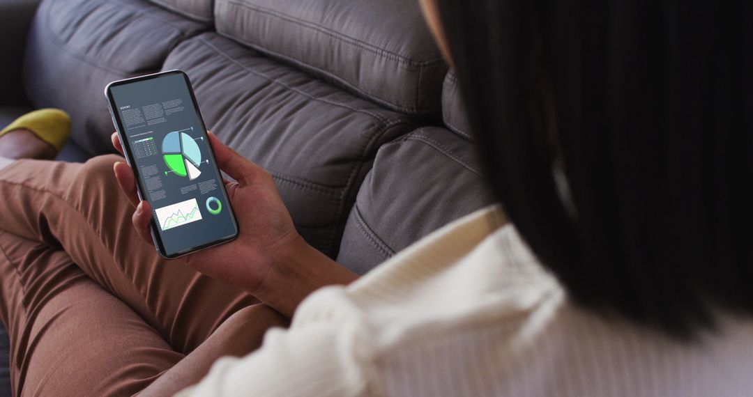 Woman Analyzing Data on Smartphone While Relaxing on Sofa