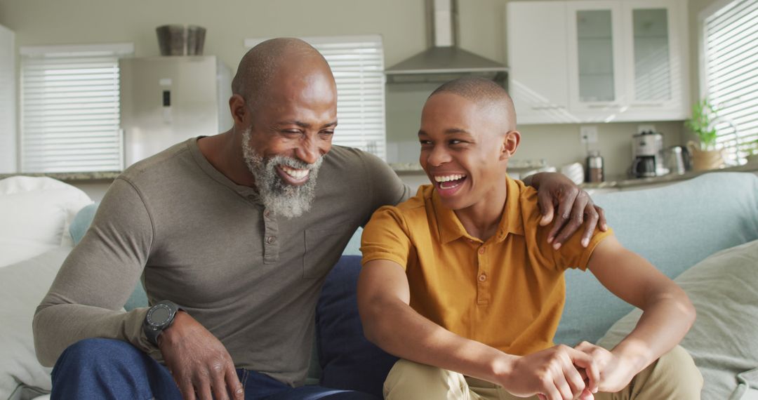 Image of happy african american father and son sitting on sofa and laughing - Free Images, Stock Photos and Pictures on Pikwizard.com