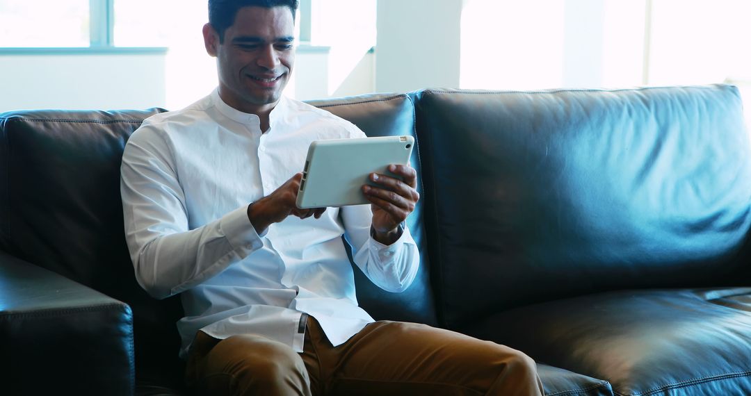 Smiling Man Using Tablet on Leather Sofa in Bright Room - Free Images, Stock Photos and Pictures on Pikwizard.com