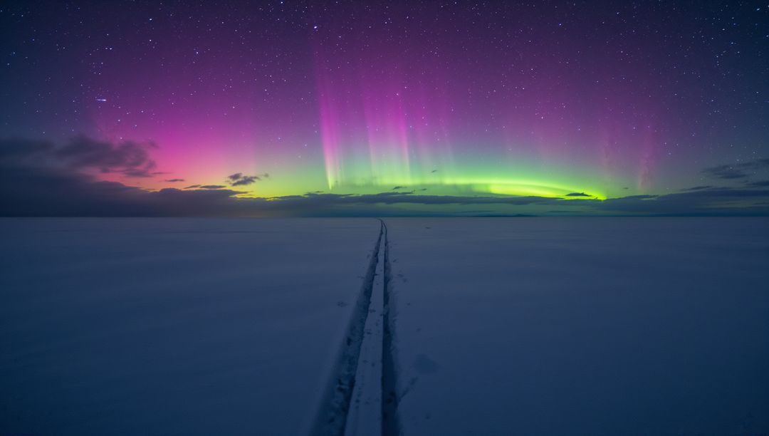 Aurora Borealis Casting Colorful Light over Frozen Plain with Parallel Tracks to Horizon