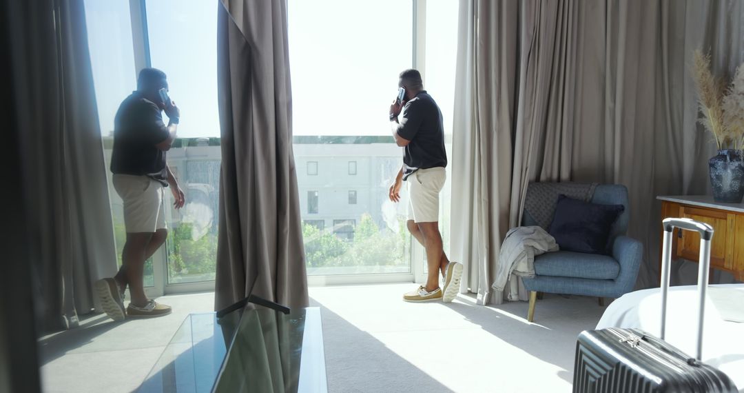 Man Standing by Hotel Window on Phone, Enjoying Urban View