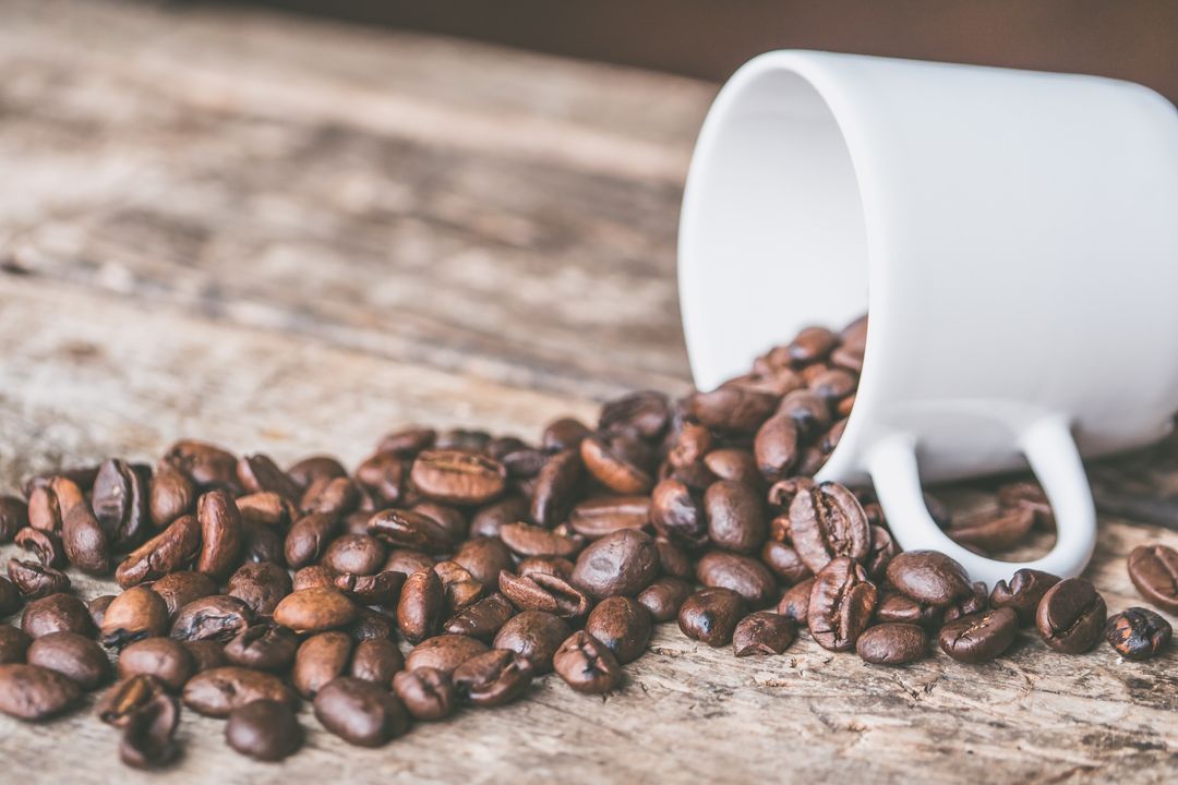 Coffee Beans Spilling from White Cup on Rustic Table