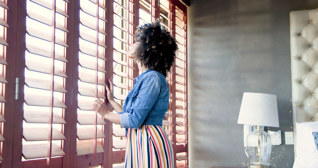 Curly-haired woman in colorful dress gazing out window with natural light