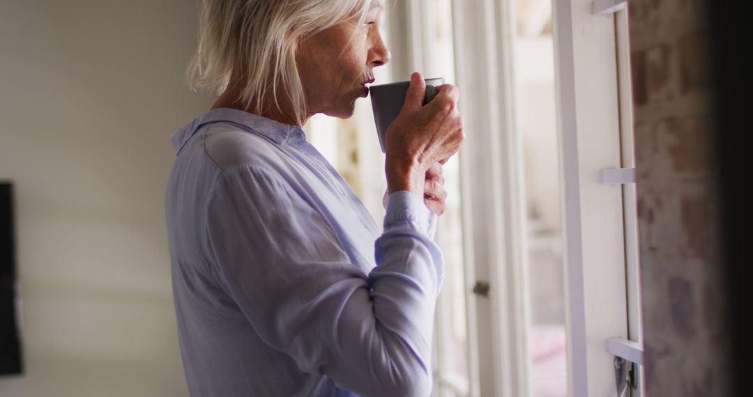 Senior Woman Drinking Coffee by Window in Relaxed Home Setting - Free Images, Stock Photos and Pictures on Pikwizard.com