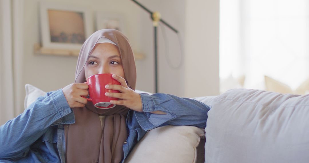 Relaxed Woman in Hijab Drinking Coffee on Sofa at Home - Free Images, Stock Photos and Pictures on Pikwizard.com