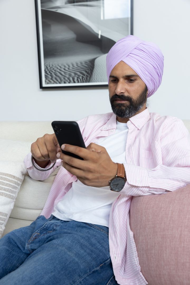 Mid Adult Man in Turban Relaxing on Couch Using Smartphone