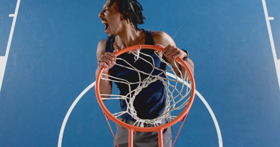 Energetic Basketball Player Hanging on the Hoop on Blue Court