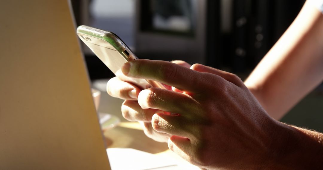 Person Using Smartphone Beside Laptop in Sunlit Room - Free Images, Stock Photos and Pictures on Pikwizard.com