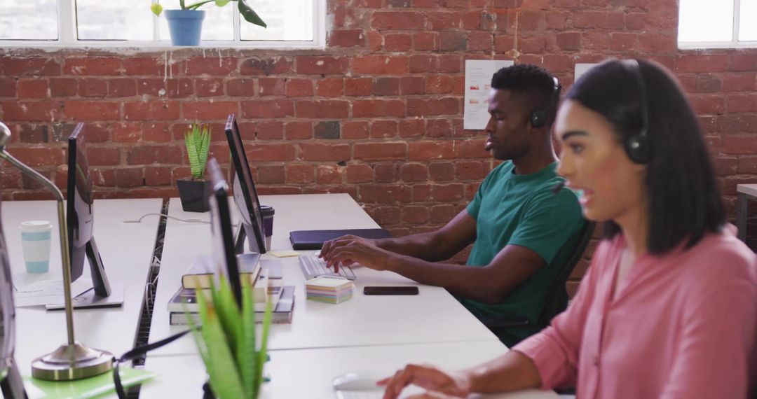 Typing professionals wearing headsets in open-plan office collaborating in modern workspace