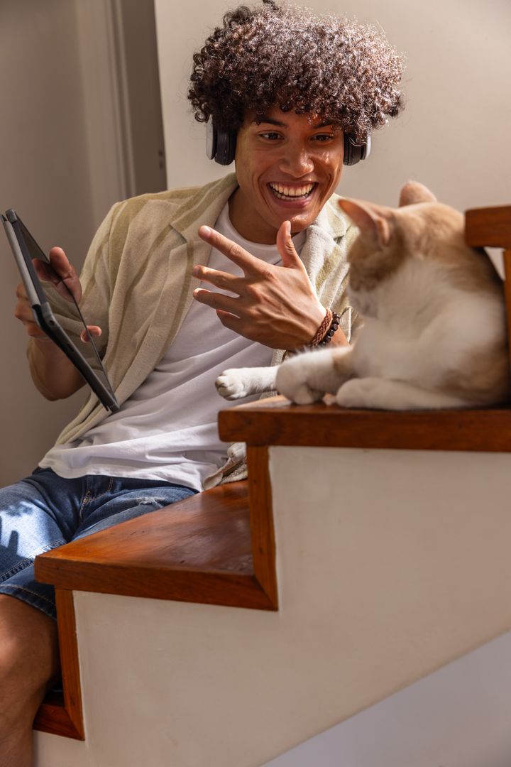 Hispanic Man Engaging with Cat on Stairs Holding Tablet