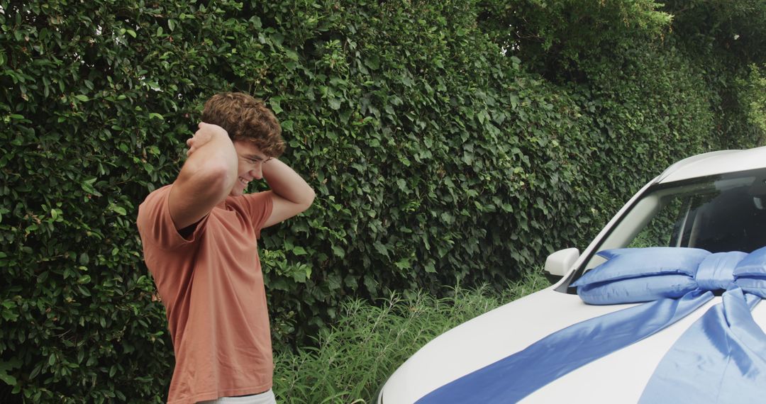 Surprised young man finding new white car with giant blue bow in driveway