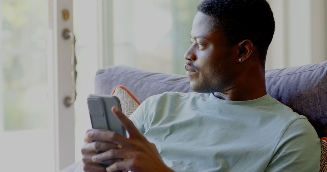 Man Relaxing with Smartphone by Window at Home