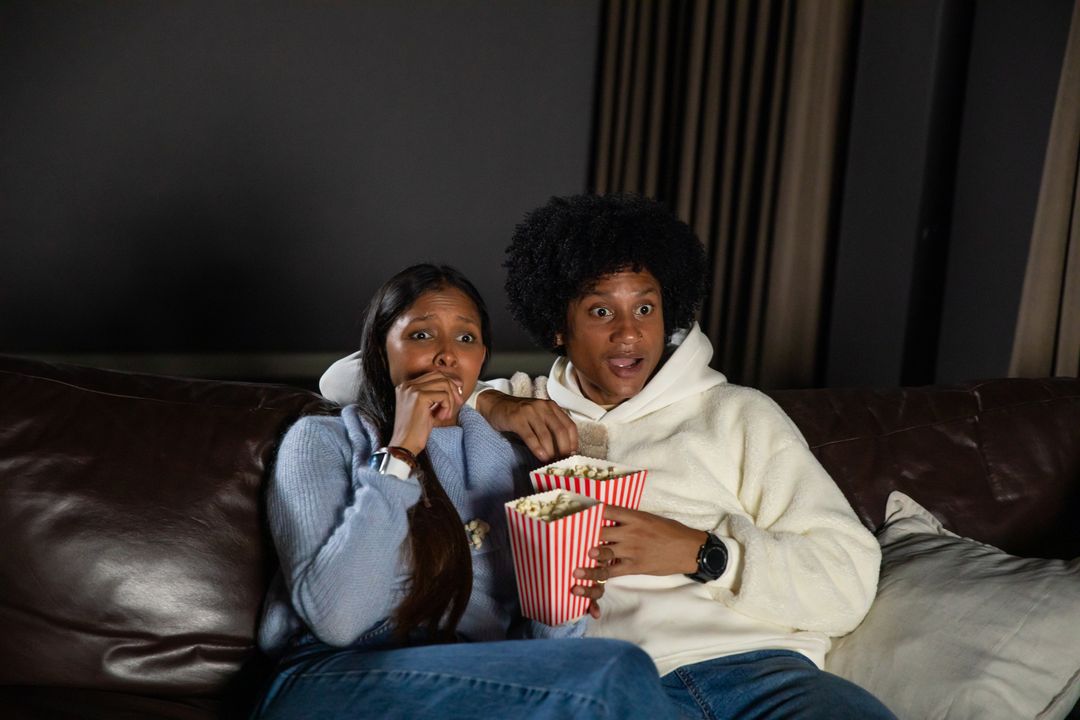 Couple Reacting to Exciting Movie with Popcorn on Sofa