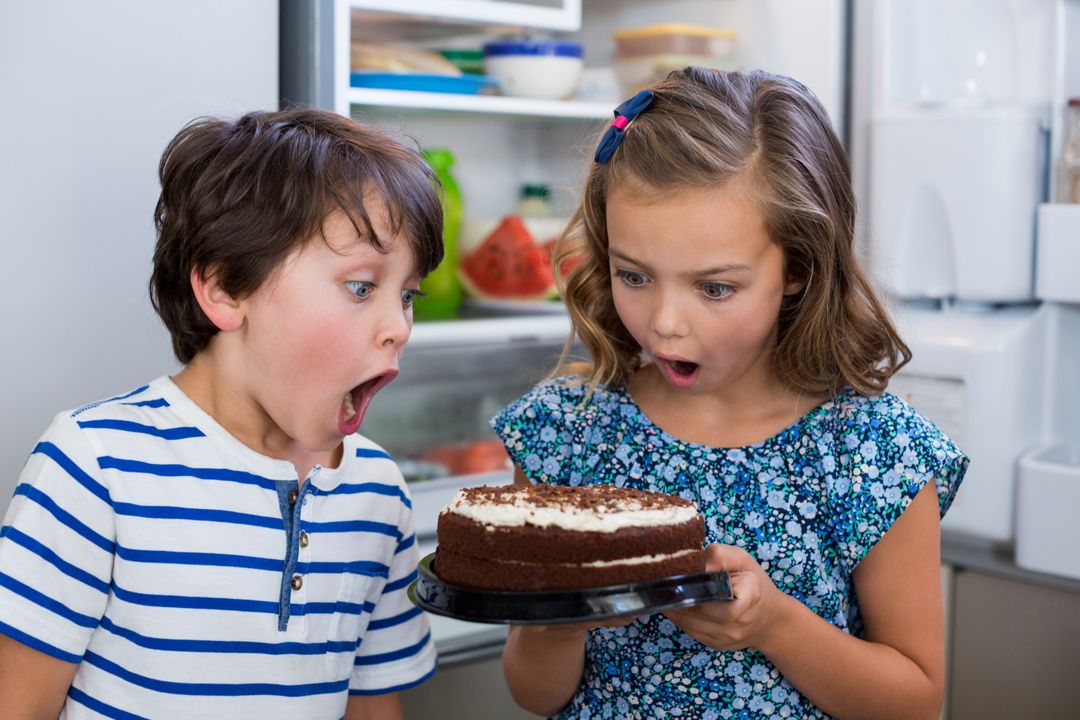 Surprised siblings looking at cake in kitchen - Free Images, Stock Photos and Pictures on Pikwizard.com