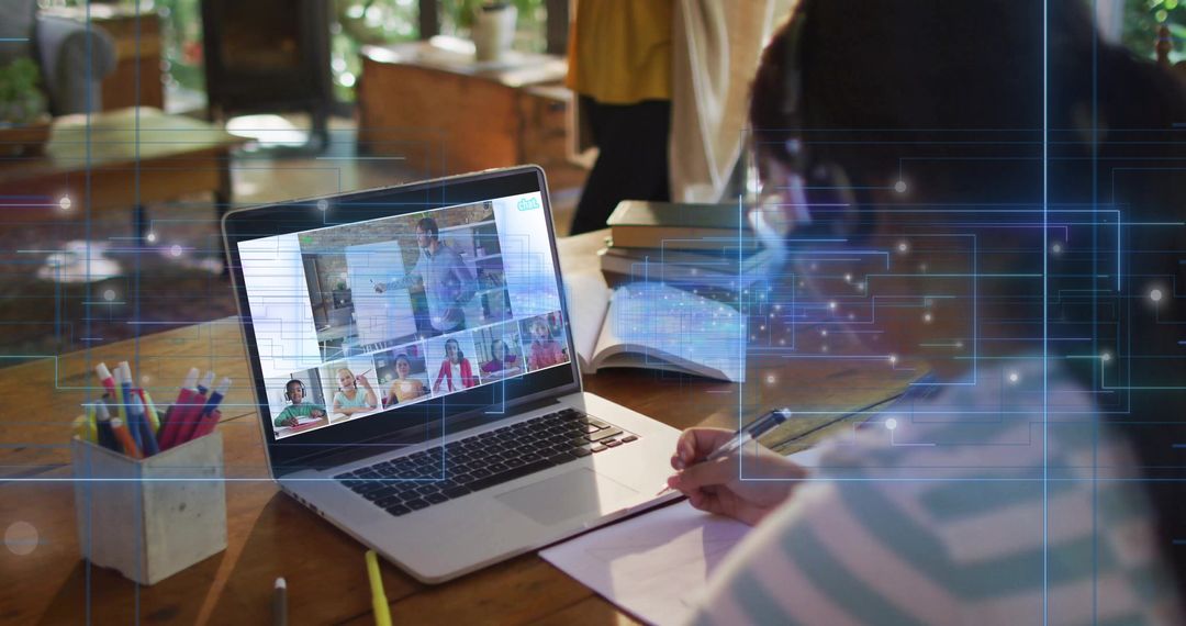 Child writing while attending virtual classroom on laptop at home with notebook and pencils