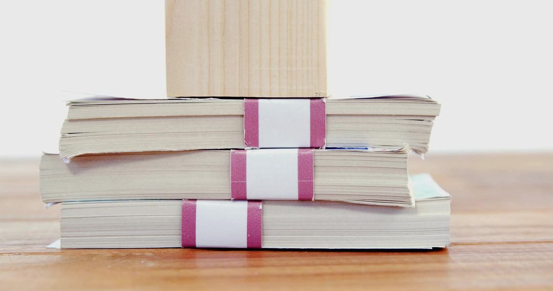 Stacked paperback bundles with magenta bands and wooden block on minimalist wood surface