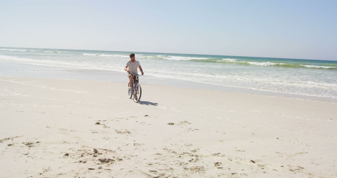 A young Caucasian man rides a bicycle along the shore on a sunny beach day, with copy space - Free Images, Stock Photos and Pictures on Pikwizard.com