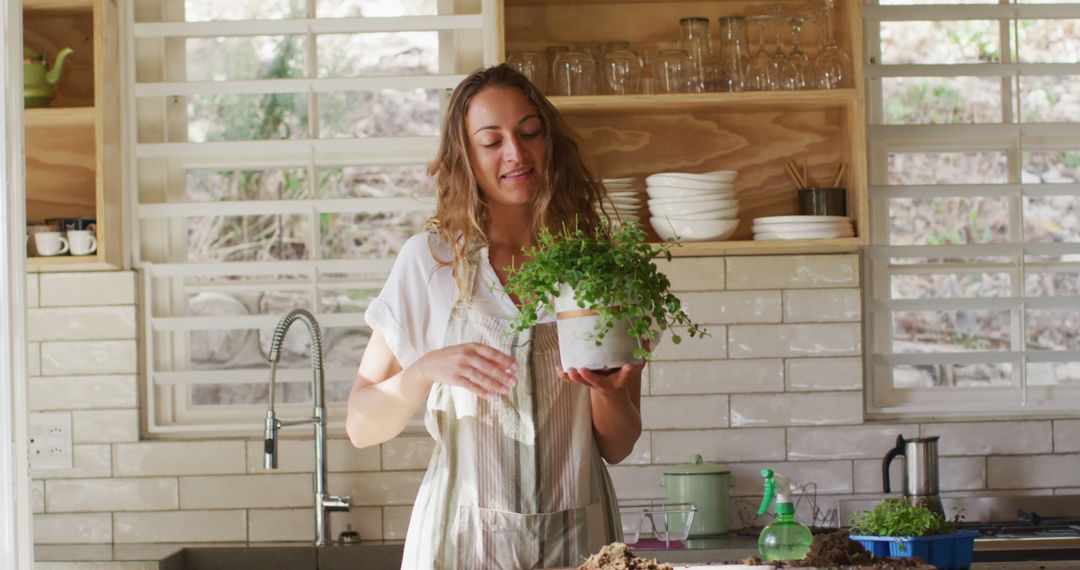 Smiling Woman Holding Plant in Modern Kitchen - Free Images, Stock Photos and Pictures on Pikwizard.com