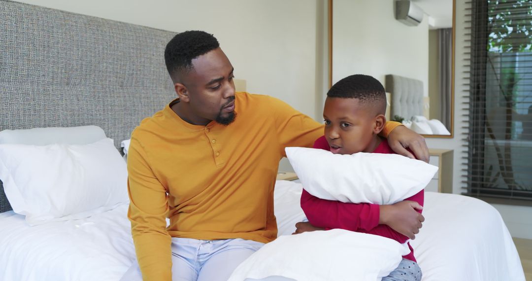 Father Comforts Son While Sitting on Bed Holding Pillow