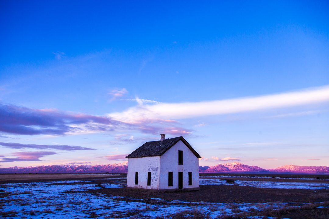 Old White House Standing on Snowy Plain at Twilight with Purple Mountain Sunset Glow