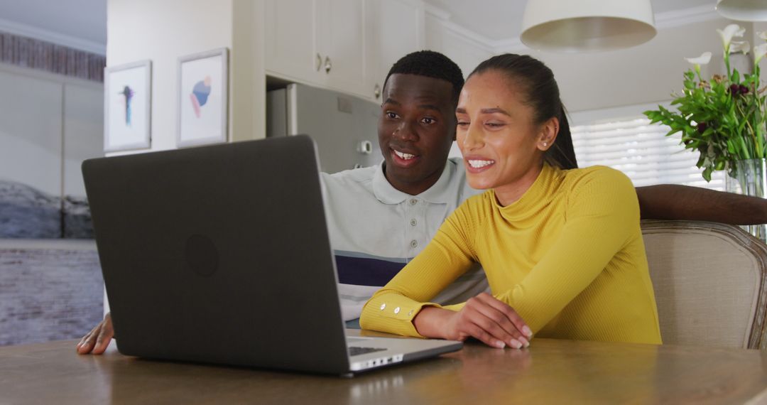 Image of happy diverse couple watching laptop together and smiling sitting in kitchen - Free Images, Stock Photos and Pictures on Pikwizard.com