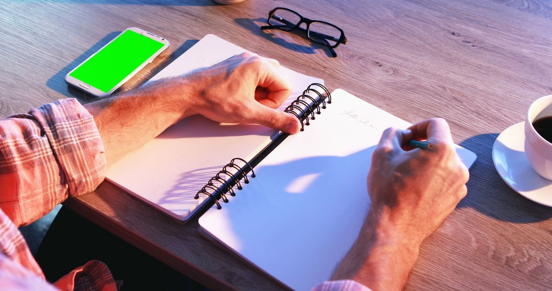 A Caucasian middle-aged man writes in a spiral notebook at a wooden desk, with copy space - Free Images, Stock Photos and Pictures on Pikwizard.com