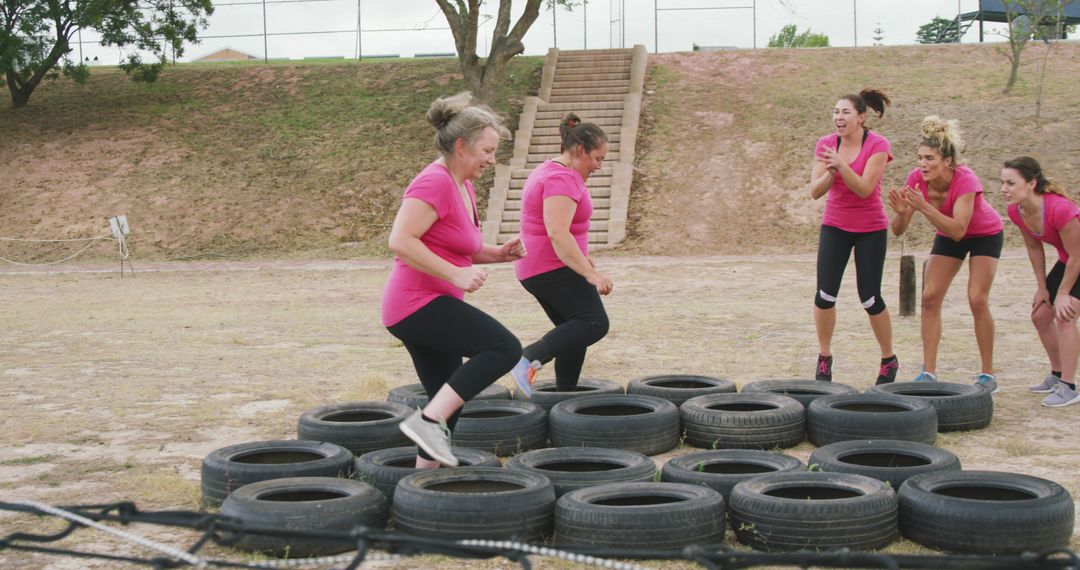 Determined caucasian female friends in pink t shirts running through tyres and cheering at bootcamp - Free Images, Stock Photos and Pictures on Pikwizard.com