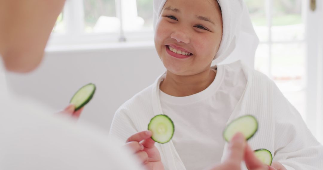 Image of happy asian mother and daughter in robes doing cucumber mask and having fun - Free Images, Stock Photos and Pictures on Pikwizard.com