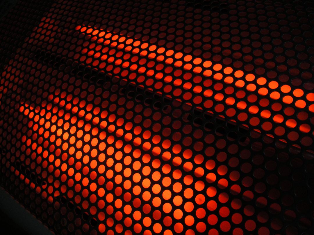 Glowing Red Infrared Heater Behind Perforated Metal Grille Creating Geometric Pattern
