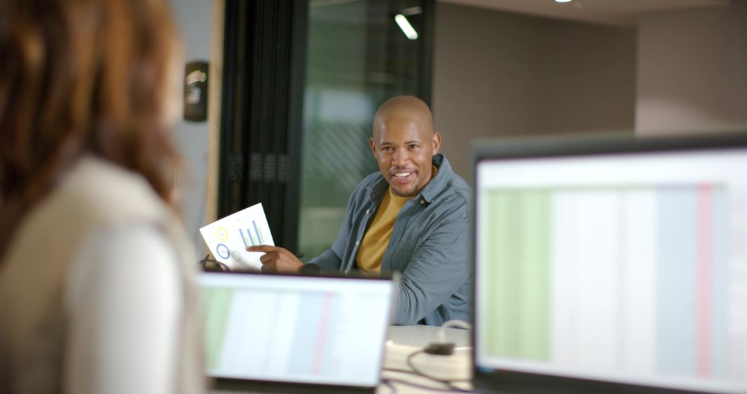 Black professional presenting data in collaborative meeting with charts, laptops, monitors