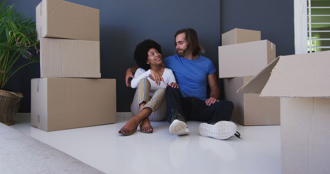 Biracial couple sitting in between cardboard boxes at new apartment house - Free Images, Stock Photos and Pictures on Pikwizard.com