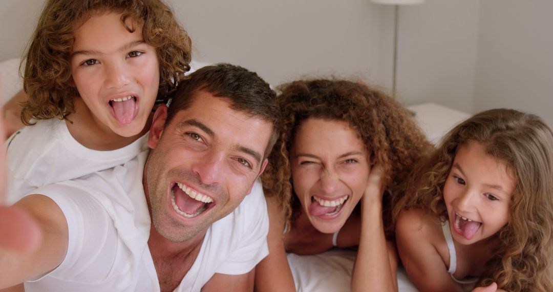 Cheerful Family Taking Selfie on Bed with Tongues Sticking Out - Free Images, Stock Photos and Pictures on Pikwizard.com