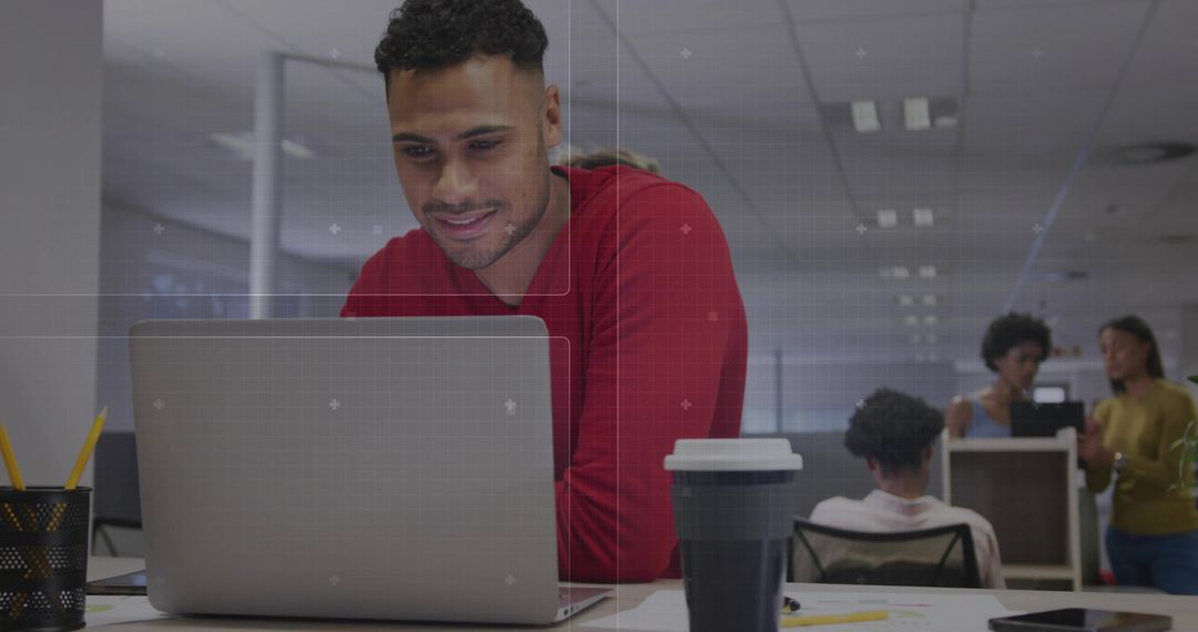 Man leaning on laptop in open-plan office collaborating with team, reusable coffee cup