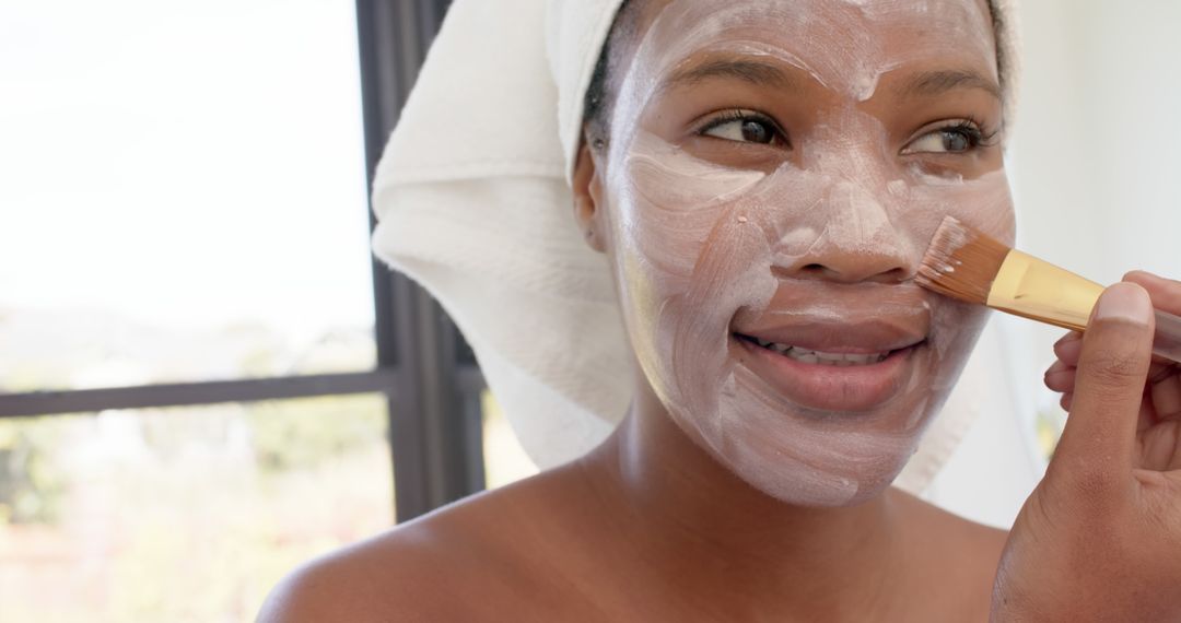 Smiling Woman Applying Face Mask with Brush in Natural Light - Free Images, Stock Photos and Pictures on Pikwizard.com